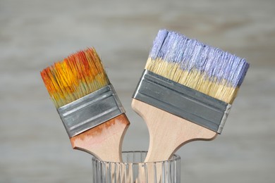 Photo of Brushes with color paints in glass on light background, closeup