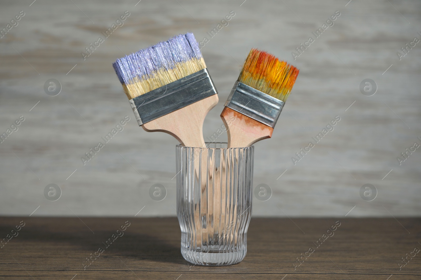 Brush with color paints in glass on wooden table Photo of Brush with color paints in glass on wooden table