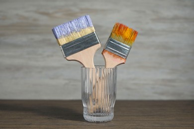 Photo of Brush with color paints in glass on wooden table