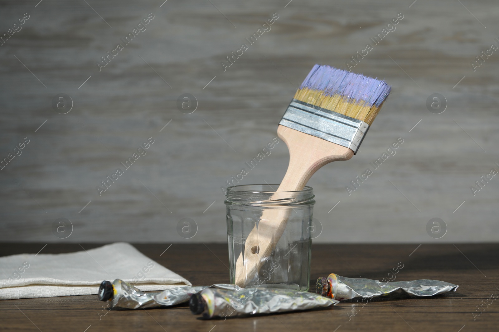 Brush in jar and paints on wooden table. Space for text Photo of Brush in jar and paints on wooden table. Space for text