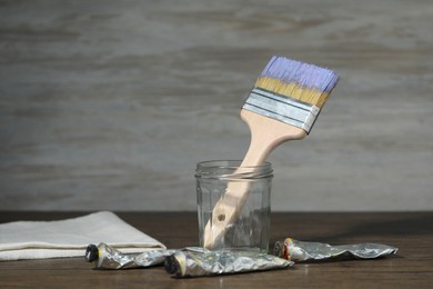 Photo of Brush in jar and paints on wooden table. Space for text
