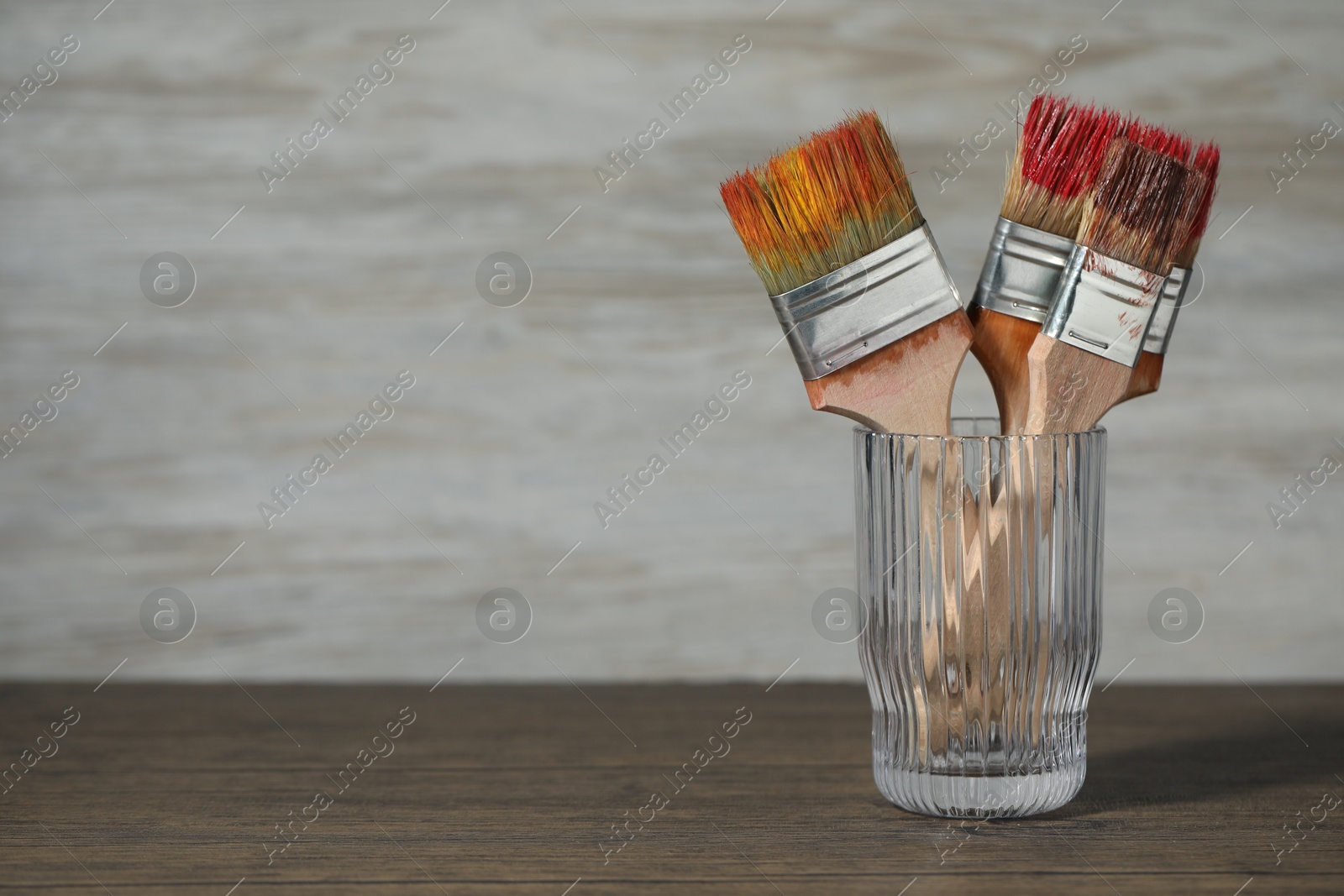 Brush with color paints in glass on wooden table. Space for text Photo of Brush with color paints in glass on wooden table. Space for text
