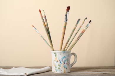 Photo of Brush with color paints in cup on wooden table