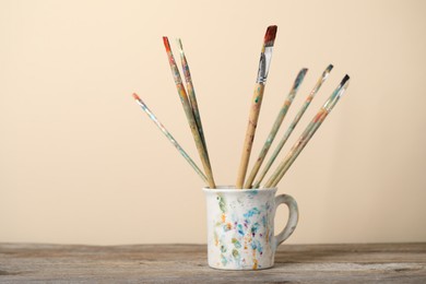 Photo of Brush with color paints in cup on wooden table