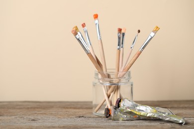 Photo of Brushes in jar and color paints on wooden table