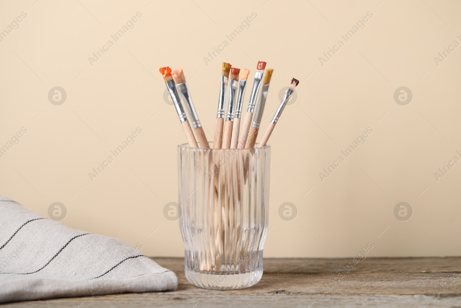 Brush with color paints in glass on wooden table Photo of Brush with color paints in glass on wooden table