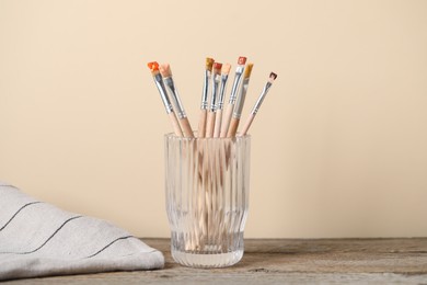 Photo of Brush with color paints in glass on wooden table