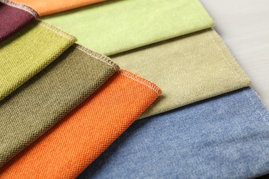 Photo of Samples of different fabrics on light wooden table, closeup