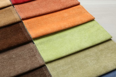 Photo of Samples of different fabrics on light wooden table, closeup