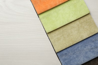 Photo of Samples of different fabrics on light wooden table, top view. Space for text