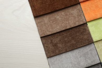 Photo of Samples of different fabrics on light wooden table, top view. Space for text