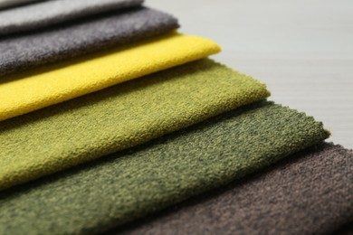 Photo of Samples of different fabrics on light wooden table, closeup
