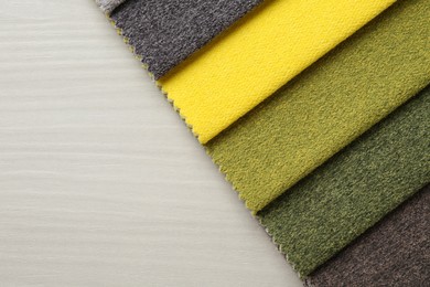 Photo of Samples of different fabrics on light wooden table, top view. Space for text