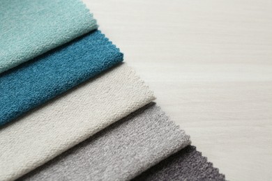Photo of Samples of different fabrics on light wooden table, closeup. Space for text