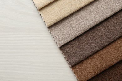 Photo of Samples of different fabrics on light wooden table, top view. Space for text