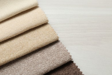 Photo of Samples of different fabrics on light wooden table, closeup