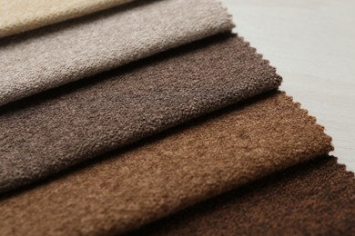 Photo of Samples of different fabrics on light wooden table, closeup