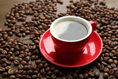 Photo of Aromatic coffee in cup and beans on wooden table, closeup