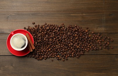 Photo of Aromatic coffee in cup, beans and cinnamon on wooden table, flat lay