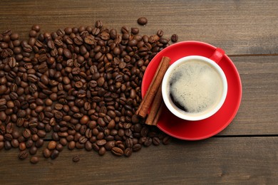 Photo of Aromatic coffee in cup, beans and cinnamon on wooden table, flat lay