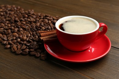 Photo of Aromatic coffee in cup, beans and cinnamon on wooden table, closeup