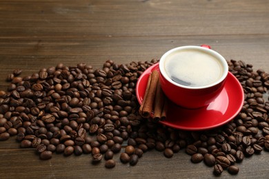 Photo of Aromatic coffee in cup, beans and cinnamon on wooden table, closeup