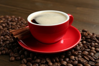 Photo of Aromatic coffee in cup, beans and cinnamon on wooden table, closeup