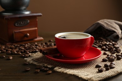 Photo of Aromatic coffee in cup, beans, cinnamon and grinder on wooden table, closeup
