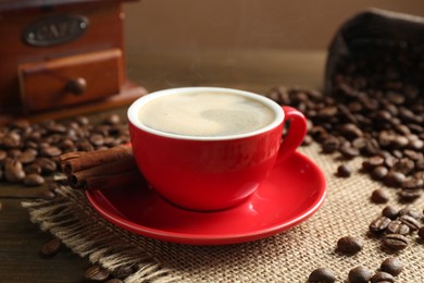 Photo of Aromatic coffee in cup, beans, cinnamon and grinder on wooden table, closeup