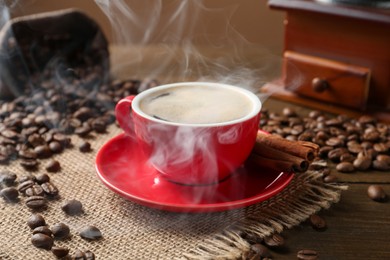 Photo of Aromatic coffee in cup, beans, cinnamon and grinder on wooden table, closeup