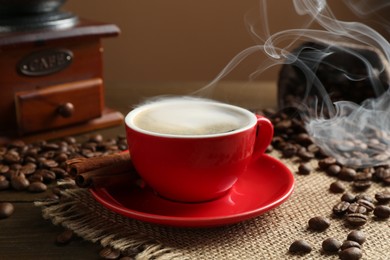 Photo of Aromatic coffee in cup, beans, cinnamon and grinder on wooden table, closeup