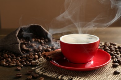 Photo of Aromatic coffee in cup, beans and cinnamon on wooden table, closeup