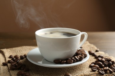 Photo of Aromatic coffee in cup and beans on table, closeup