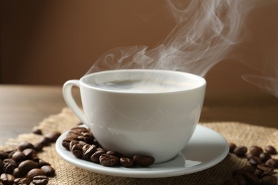 Photo of Aromatic coffee in cup and beans on table, closeup