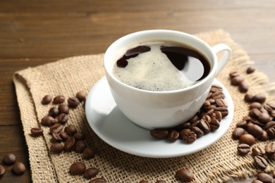 Photo of Aromatic coffee in cup and beans on wooden table, closeup