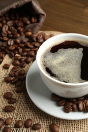 Photo of Aromatic coffee in cup and beans on table, closeup