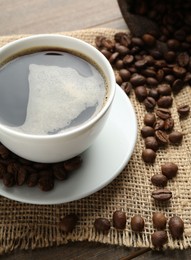 Photo of Aromatic coffee in cup and beans on wooden table, above view