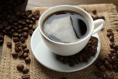 Photo of Aromatic coffee in cup and beans on table, closeup