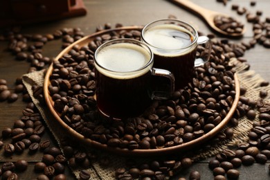 Photo of Aromatic coffee in cups and beans on wooden table, closeup