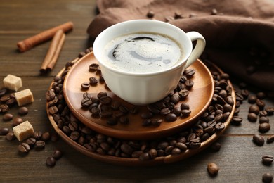 Photo of Aromatic coffee in cup, beans, brown sugar and cinnamon on wooden table, closeup
