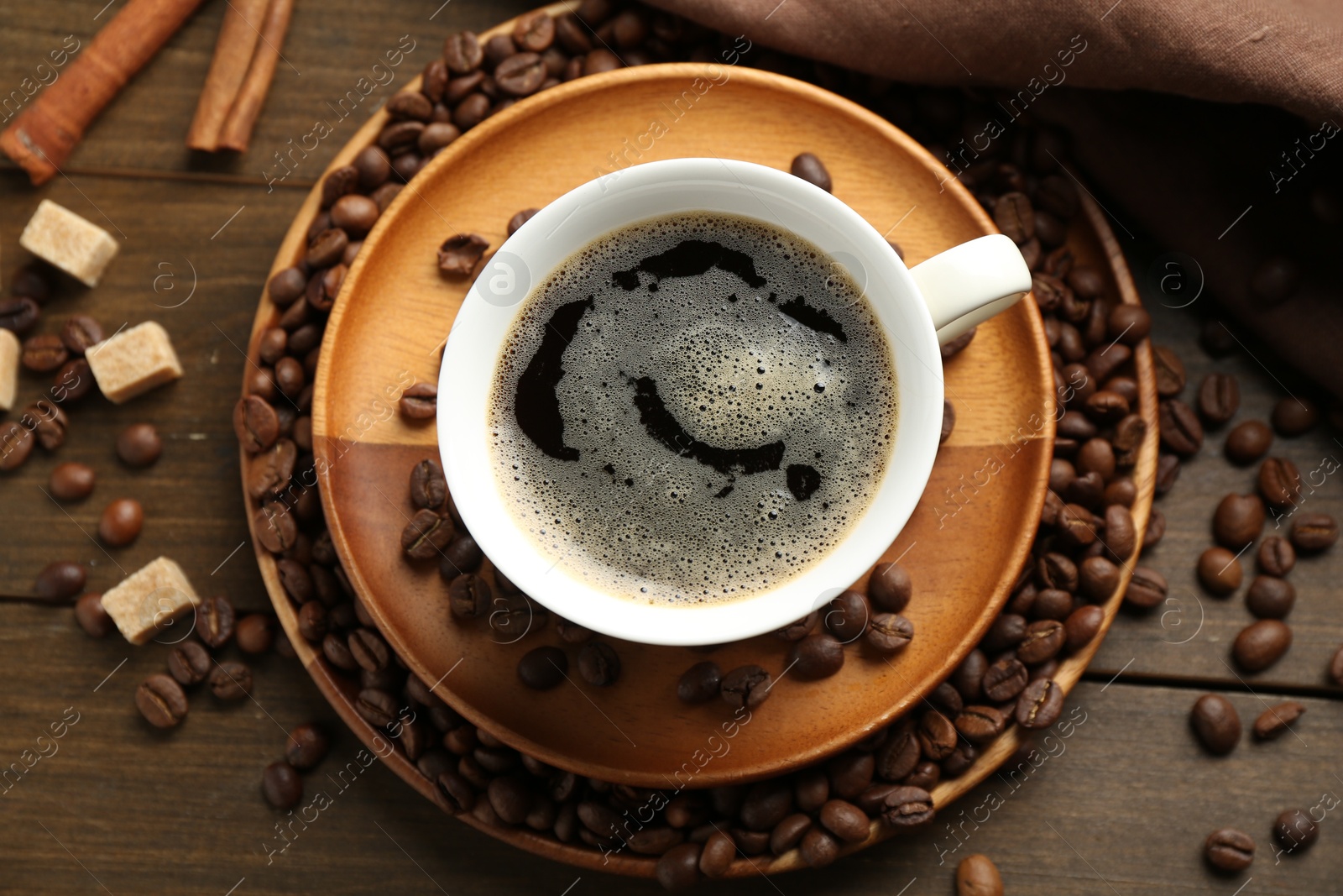 Aromatic coffee in cup, beans, brown sugar and cinnamon on wooden table, flat lay Photo of Aromatic coffee in cup, beans, brown sugar and cinnamon on wooden table, flat lay