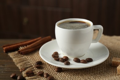 Photo of Aromatic coffee in cup, beans, brown sugar and cinnamon on wooden table, closeup