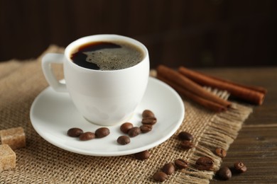 Photo of Aromatic coffee in cup, beans, brown sugar and cinnamon on wooden table, closeup
