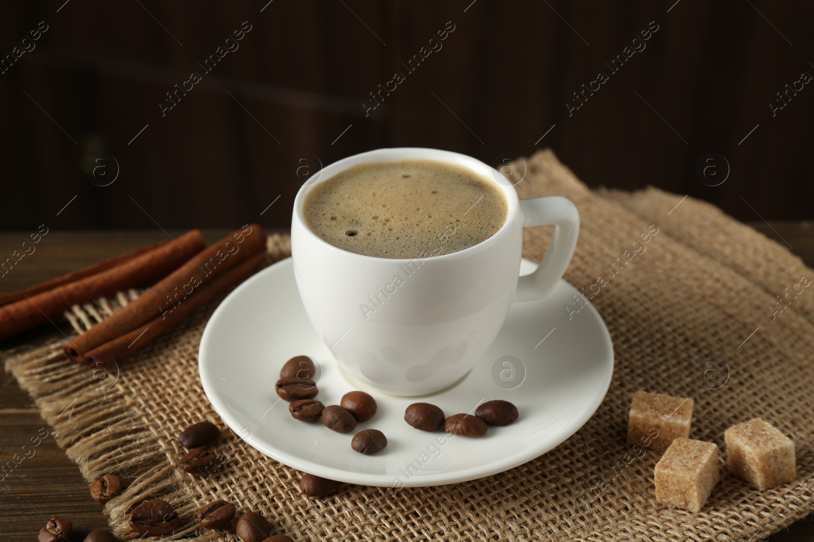 Aromatic coffee in cup, beans, brown sugar and cinnamon on table, closeup Photo of Aromatic coffee in cup, beans, brown sugar and cinnamon on table, closeup