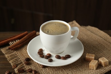 Photo of Aromatic coffee in cup, beans, brown sugar and cinnamon on table, closeup