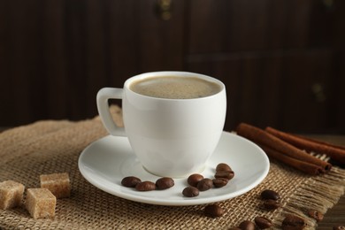 Photo of Aromatic coffee in cup, beans, brown sugar and cinnamon on table, closeup