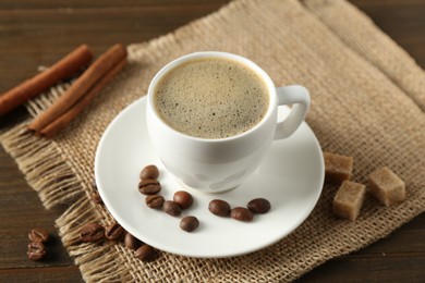 Photo of Aromatic coffee in cup, beans, brown sugar and cinnamon on wooden table, closeup