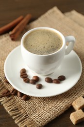 Photo of Aromatic coffee in cup, beans, brown sugar and cinnamon on table, closeup