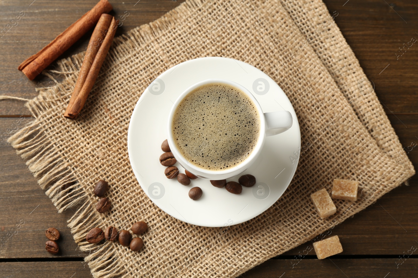 Aromatic coffee in cup, beans, brown sugar and cinnamon on wooden table, flat lay Photo of Aromatic coffee in cup, beans, brown sugar and cinnamon on wooden table, flat lay