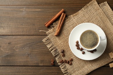 Photo of Aromatic coffee in cup, beans, brown sugar and cinnamon on wooden table, flat lay. Space for text